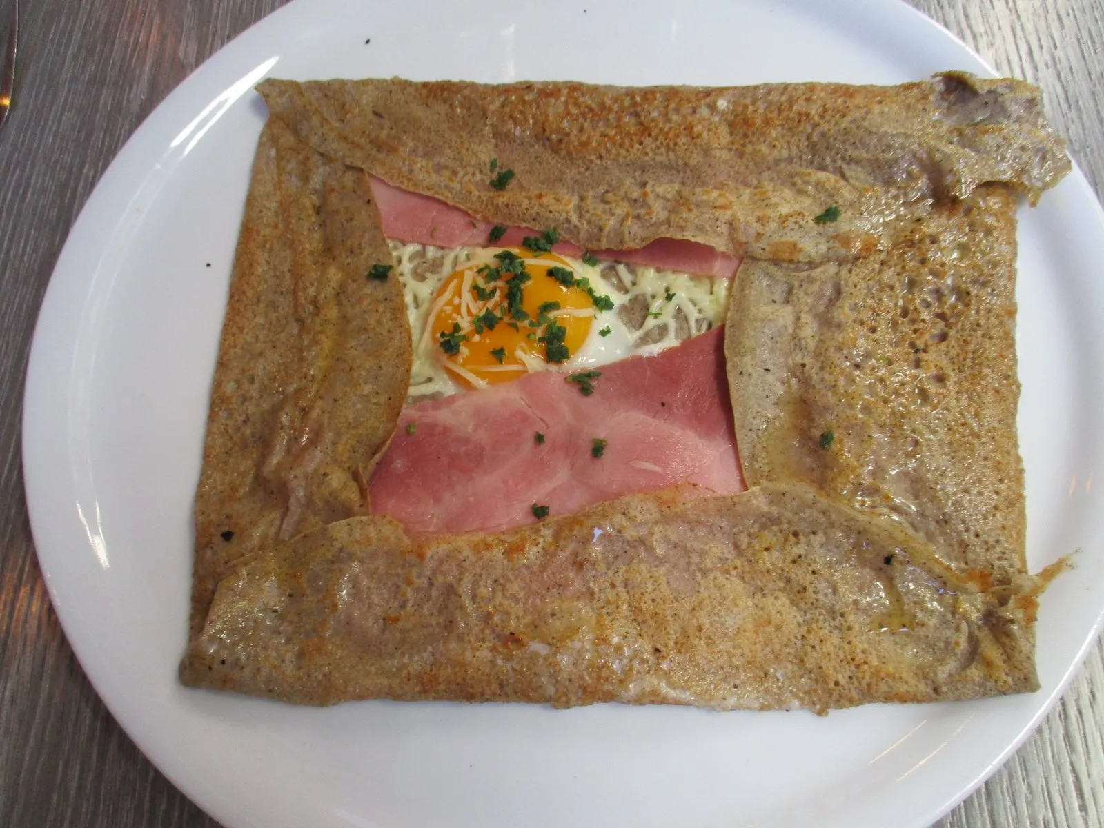Buckwheat galette complète with ham, egg and cheese, folded into a square on a plate